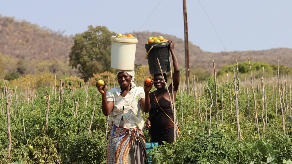 Two women on a field carrying buckets over their head